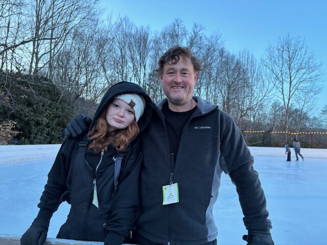 Father and daughter posing for a picture on an ice rink.